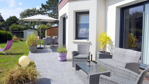 An outdoor patio with wicker furniture, a glass table, and potted plants. - Holiday Home in Crozon near Sandy Beaches (Crozon)