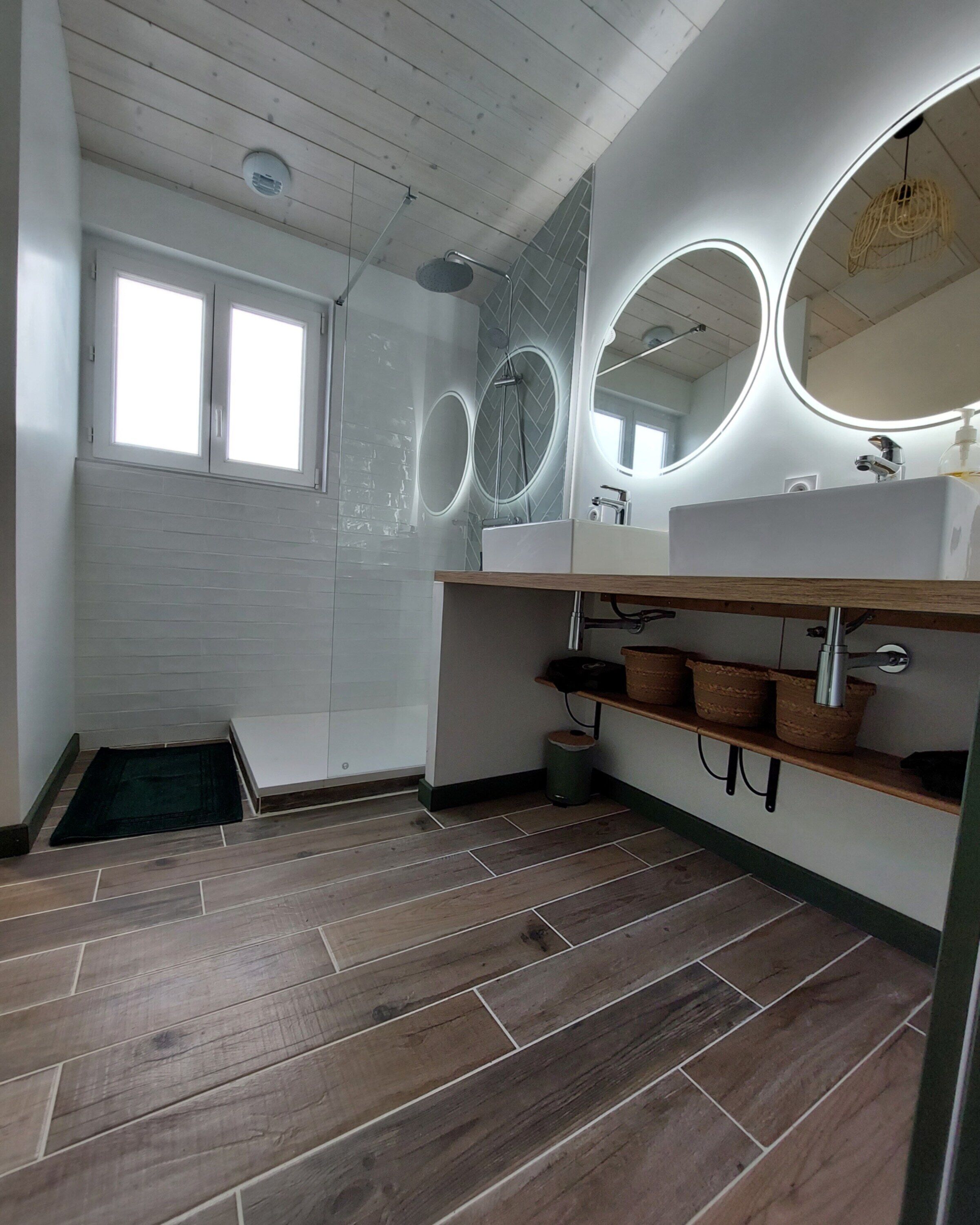 Une salle de bain moderne avec une douche, deux lavabos et un grand miroir.