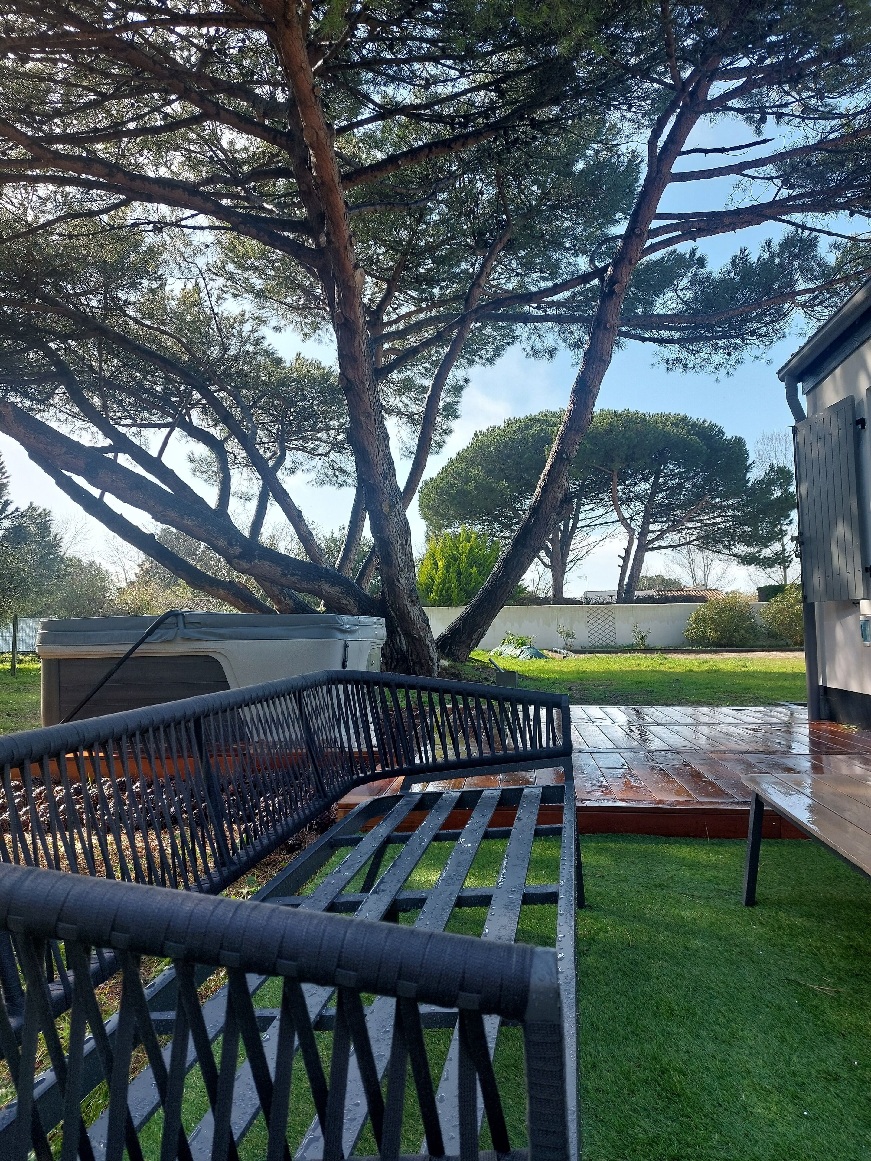 A wooden deck with a metal bench, surrounded by lush green grass and trees.