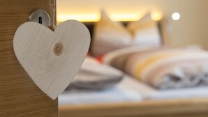 Eine Holztür mit Herz-Dekoration und ein Bett mit Kissen und Decke im Hintergrund.