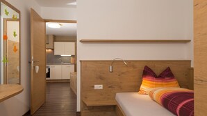 Ein kompakter Raum mit einem Bett, einer kleinen Küchenzeile und einer Tür zu einem weiteren Raum.