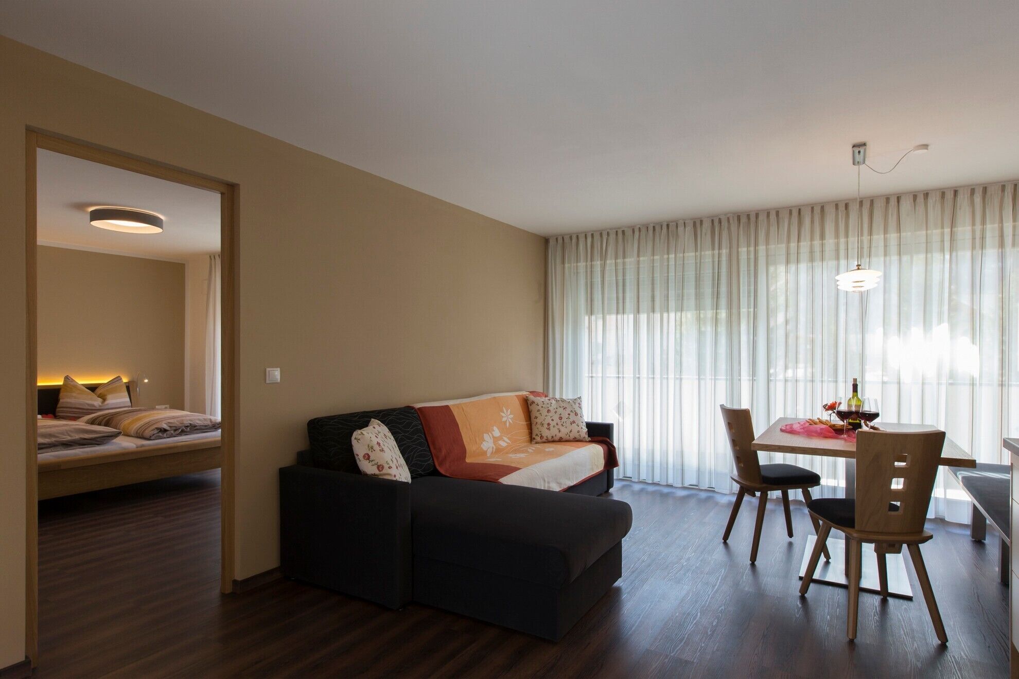 Un salon avec un canapé, une table à manger et des chaises, un miroir et une fenêtre avec des rideaux.