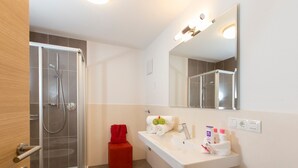 Ein modernes Badezimmer mit einer Duschkabine aus Glas, einem weißen Waschbecken mit Pflegeprodukten und einem Spiegel darüber.