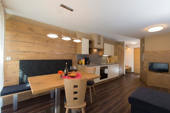 Une cuisine moderne avec des meubles en bois, un coin repas avec un banc et un téléviseur dans le salon.