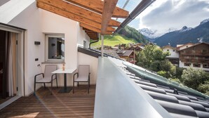 A balcony with a table and chairs, a window, and a view of a mountain landscape.