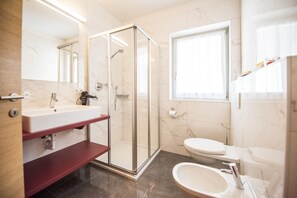 Un baño moderno con ducha envuelta en vidrio, lavamanos con encimera de mármol y un inodoro.