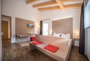 Un dormitorio moderno con cabecera de madera, cama con cojines rojos, mesita de noche y un cuadro en la pared.