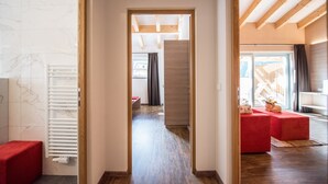 A hallway with a wooden ceiling, a red bench, and a view into a room with a window and a red sofa.