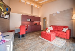 Un salon moderne avec un canapé rouge, un coin repas avec une chaise rouge et une cuisine équipée d’un four à micro-ondes.