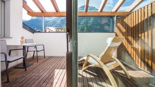Un balcon avec un plancher en bois, une table avec des chaises et un fauteuil.