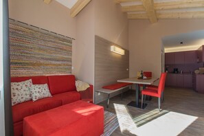 A modern living space with a red sofa, a dining table with red chairs, a kitchen area, and a wall with a colorful woven tapestry.