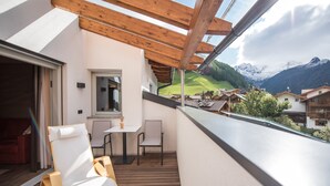 Un balcon avec des poutres en bois, une table, deux chaises et une vue sur des montagnes enneigées.