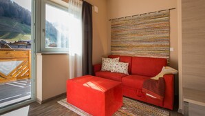 Un salon moderne avec un canapé rouge, un tapis à motifs et une vue sur un paysage montagneux, visible à travers une grande fenêtre.