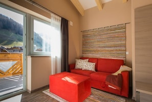 Un salon moderne avec un canapé rouge, un tapis à motifs et une vue sur un paysage montagneux, visible à travers une grande fenêtre.