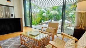 A modern living room with a glass door leading to a patio area with outdoor furniture and greenery.