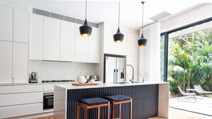 A modern kitchen with white cabinets, a central island with stools, pendant lighting, and a view of a lush garden.