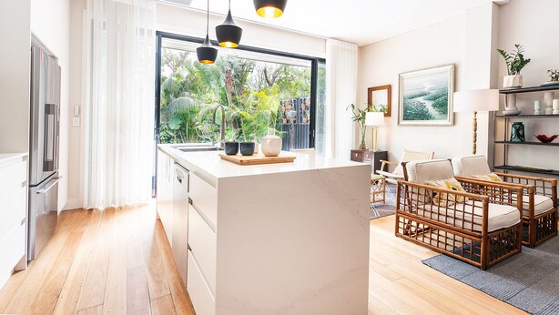 A modern kitchen with a large window, wooden flooring, and a dining area with wicker furniture.