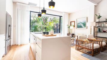 A modern kitchen with a large window, wooden flooring, and a dining area with wicker furniture.