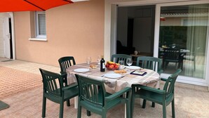 An outdoor dining area with a table set for two, surrounded by green chairs, a red umbrella, and a glass door leading to a patio. - Terraced holiday home in Moliets (Moliets)