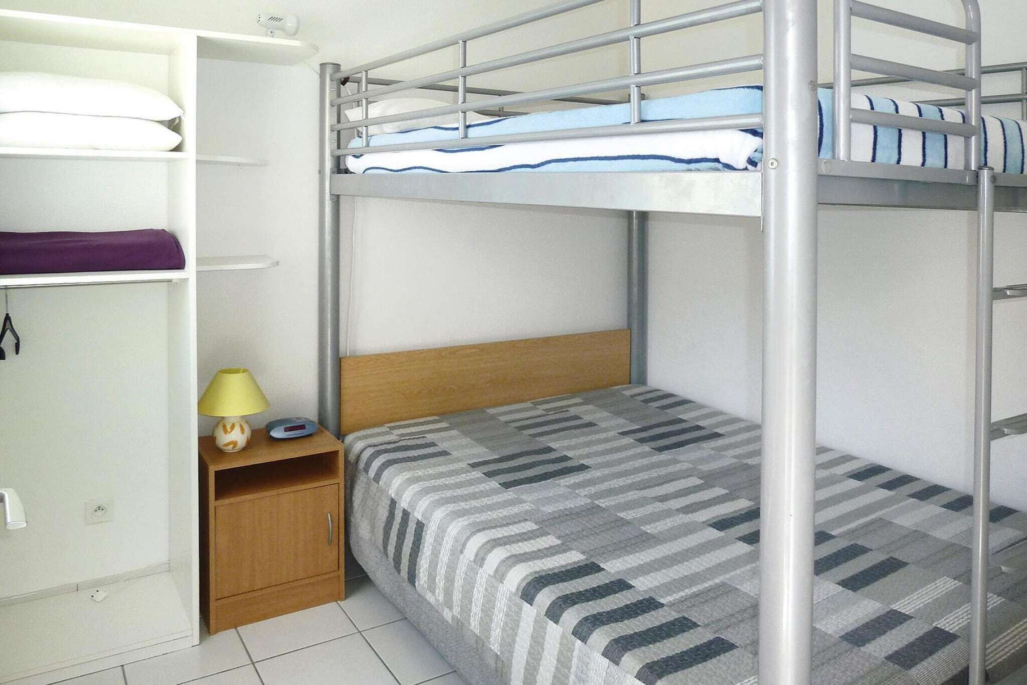 A bunk bed with a wooden headboard, a bedside table with a lamp, and a shelf with pillows.