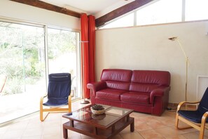 Un salón con un sofá de cuero rojo, un sillón azul, una mesa de centro de madera y una lámpara de pie.