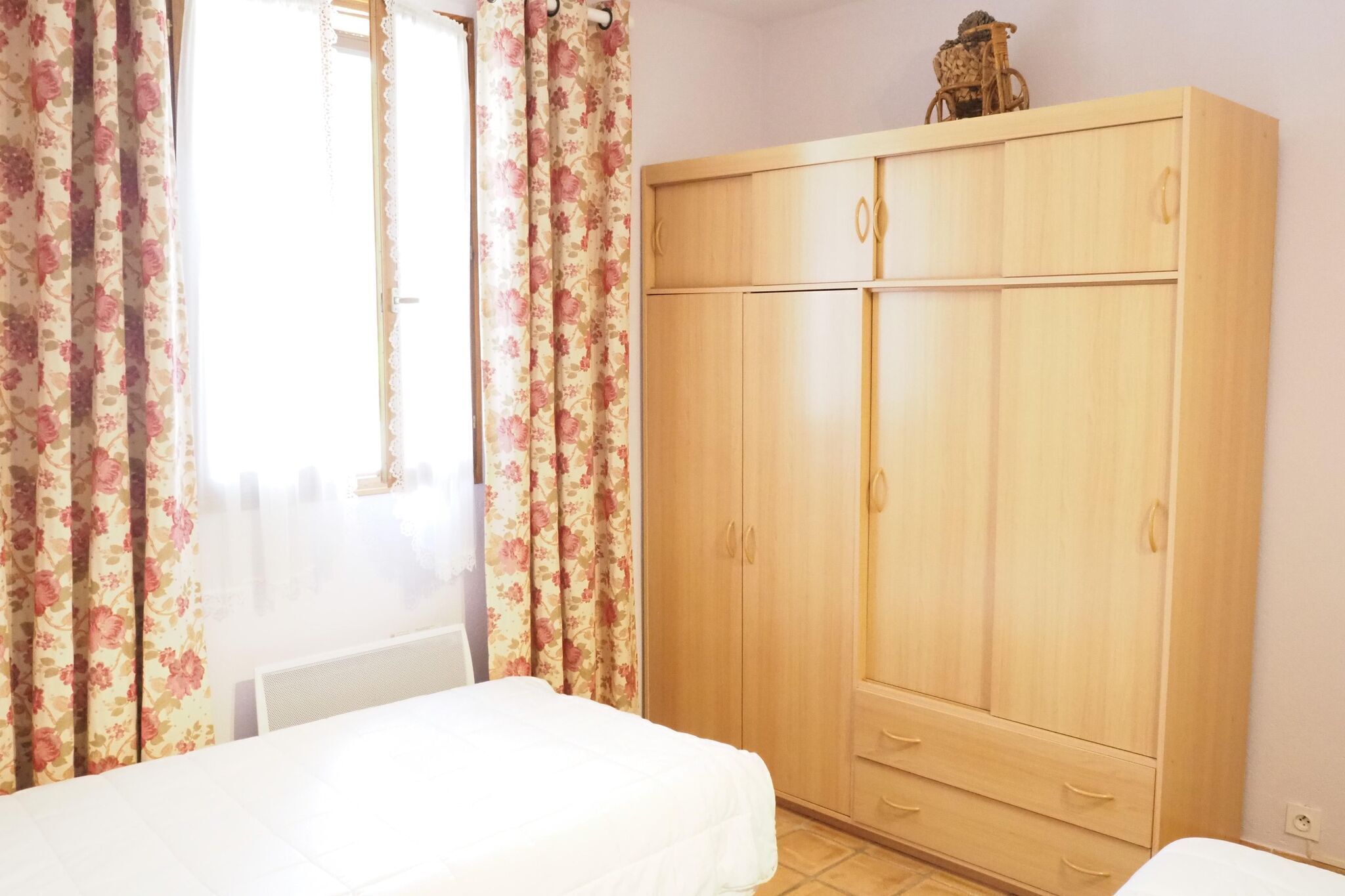 A bedroom with a wooden wardrobe, a bed, and floral curtains.
