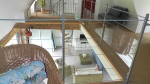 A multi-level living space with a glass railing, a sofa, a wicker chair, and a staircase. - Quiet cottage in the countryside. (Segonzac)