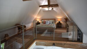 A bedroom with a sloped ceiling, a bed with a colorful quilt, two bedside tables with lamps, and a wooden chair. - Quiet cottage in the countryside. (Segonzac)