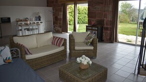 A living room with wicker furniture, a coffee table with flowers, and a view of the garden through glass doors. - Quiet cottage in the countryside. (Segonzac)