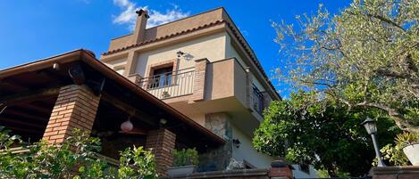 A two-story building with a balcony, a stone wall, and a clear blue sky.