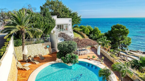 Eine moderne Villa mit Pool, umgeben von üppiger Vegetation und Blick aufs Meer.