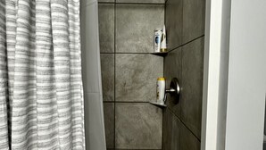 A shower area with a showerhead, a towel rack with toiletries, and a striped shower curtain.