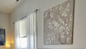 A living room with a dark-colored sofa, two black stools, a round table, and a painting of white flowers on the wall.