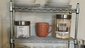 A metal shelf with various kitchen items including mugs, a candle, and glassware.