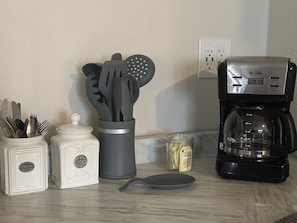 Uma bancada de cozinha com utensílios, uma cafeteira e um frasco de açúcar.