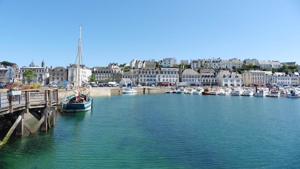 A harbor with boats docked, a prominent church spire, and a row of residential buildings.