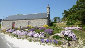 A stone church with a red door and a bell tower, surrounded by a garden with purple and yellow flowers.