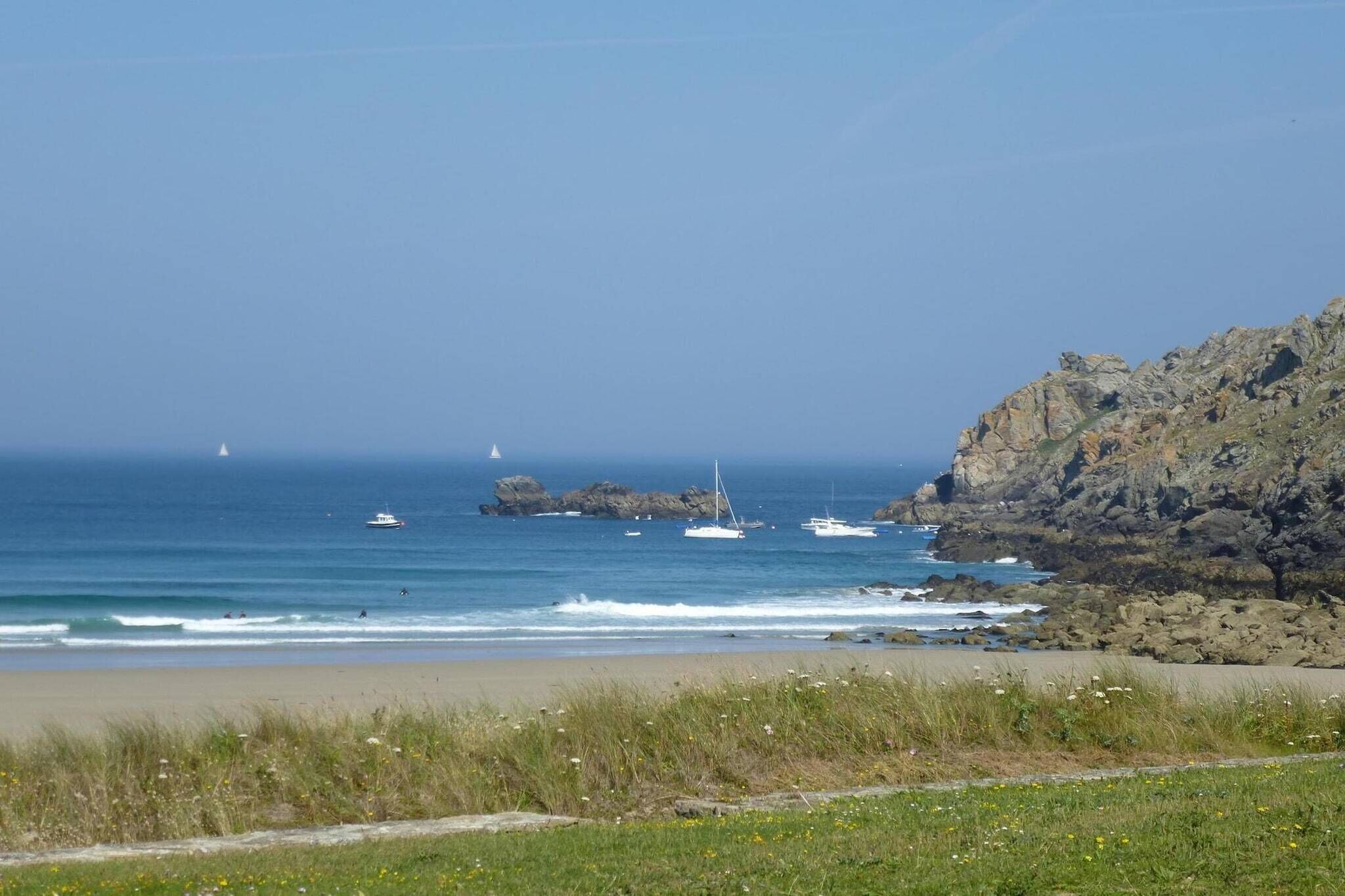 A coastal landscape with a rocky cliff, a sandy beach, and several boats in the water.