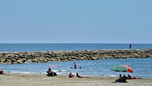 A beach with people relaxing, a rocky breakwater, and a clear sky.