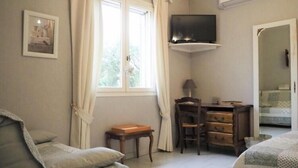 A bedroom with a bed, a desk, a chair, a television, and a window with curtains.