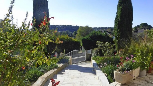 A stone pathway leading to a gate, surrounded by lush greenery and tall cypress trees.