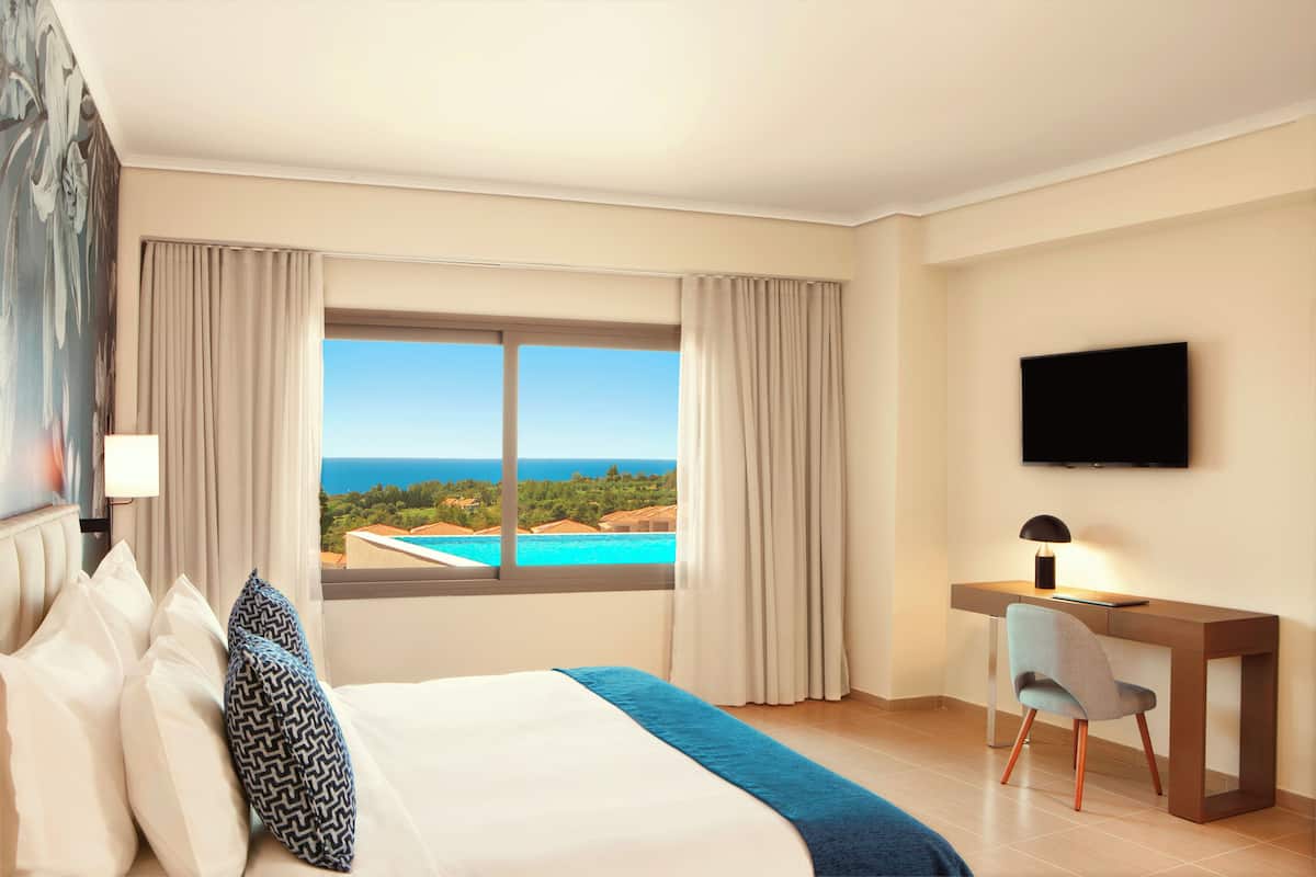Habitación de hotel con cama, escritorio, silla, televisor y vista al océano.