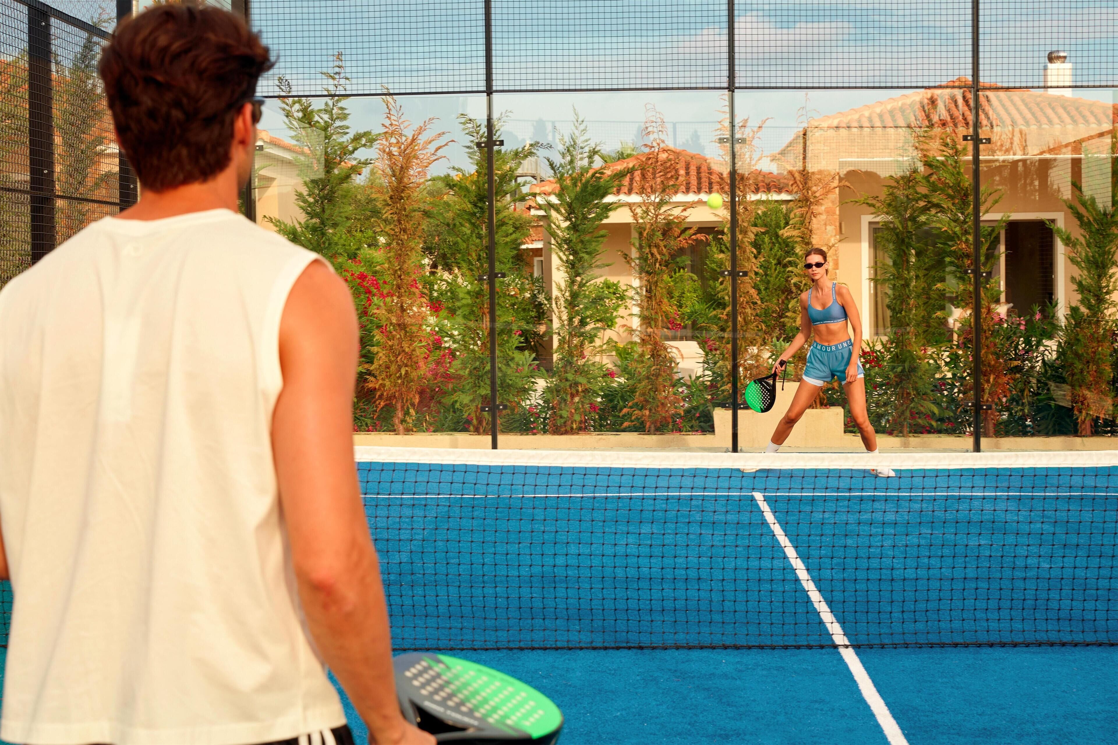 Una cancha de tenis con una red, rodeada de vegetación y edificios.