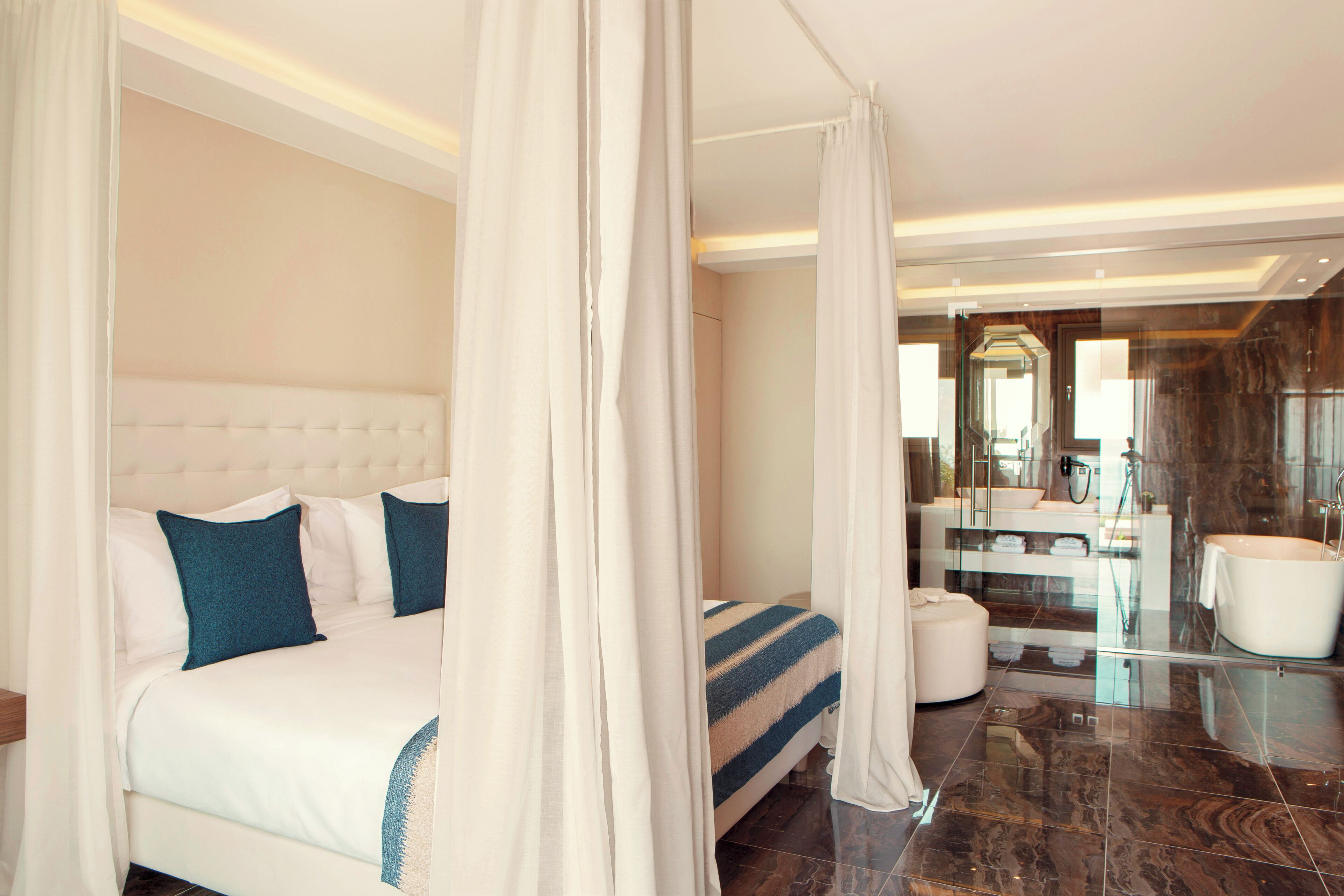 A modern hotel room with a large bed, a separate bathroom with a glass shower, and a marble floor.