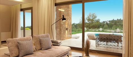 A modern living room with a sofa, a coffee table, and a view of a swimming pool and greenery.