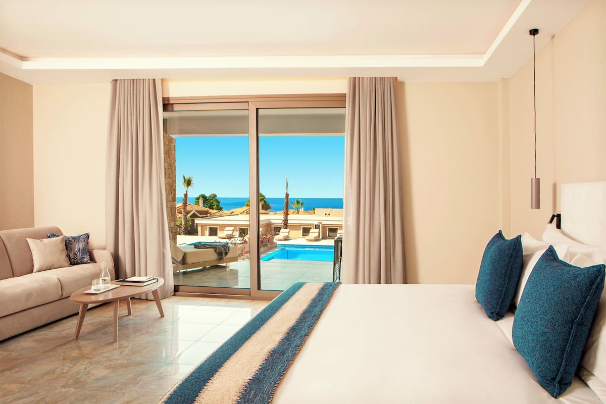 Habitación de hotel con cama, sofá, mesa de centro y vistas a una piscina y edificios.