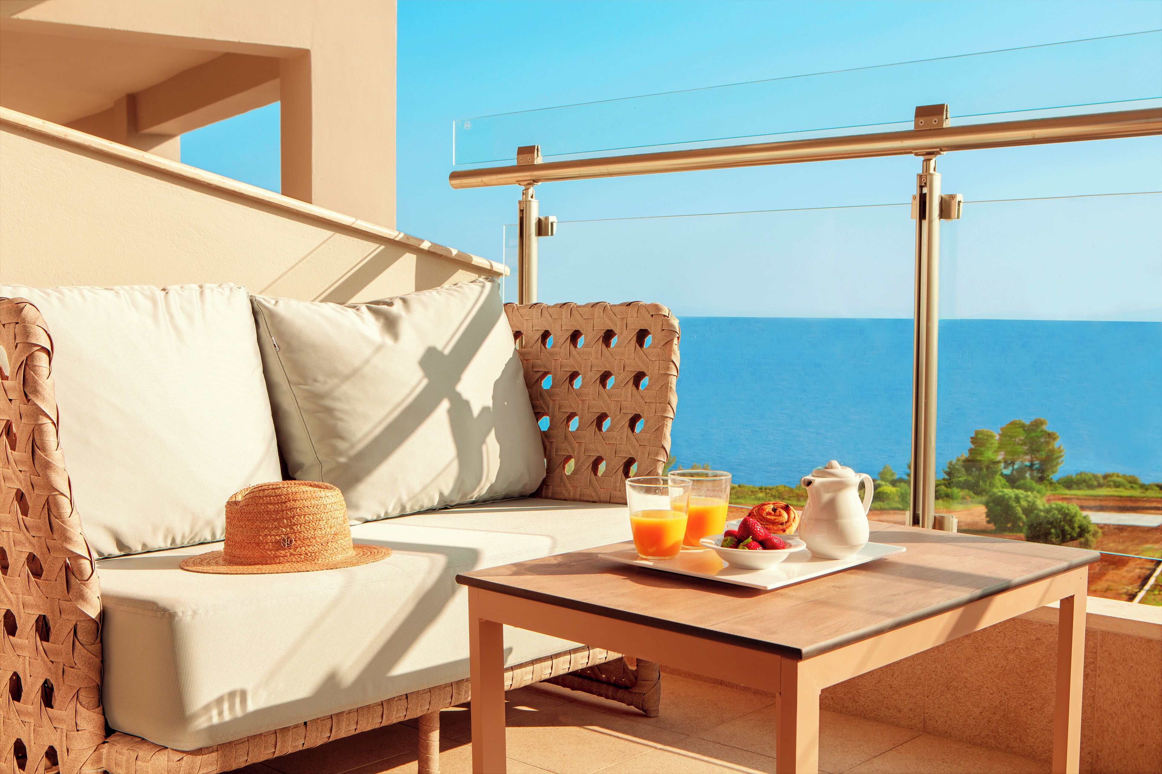 A balcony with a wicker sofa, a table with breakfast items, and a view of the sea.