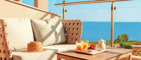 A balcony with a wicker sofa, a table with breakfast items, and a view of the sea.