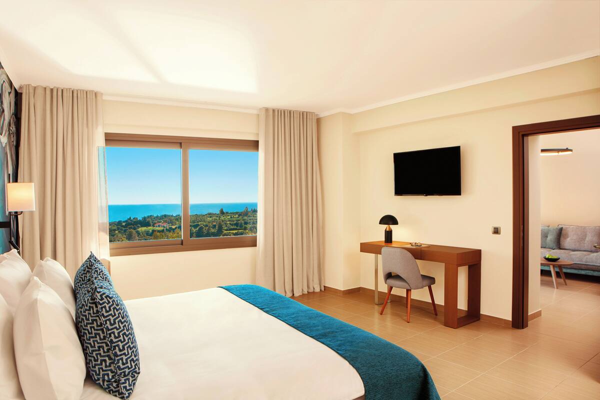 Habitación de hotel con cama, escritorio, silla, televisor y vista al mar.