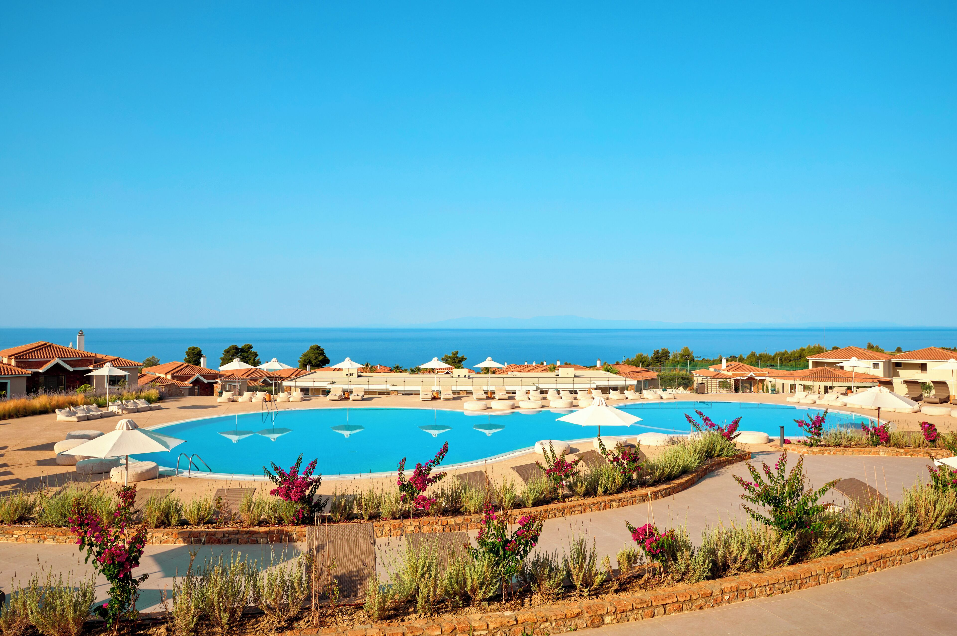A resort with a large swimming pool, multiple lounge areas, and a view of the sea.
